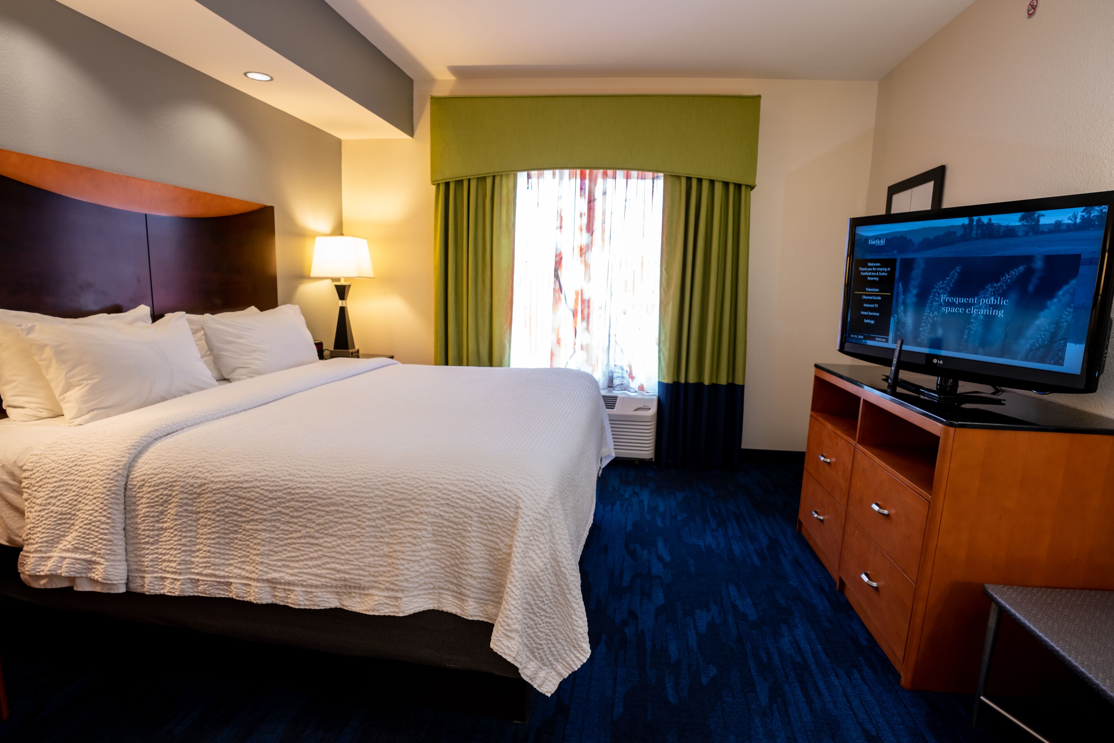 A hotel room with a large bed, a television, a desk, and a window with curtains.