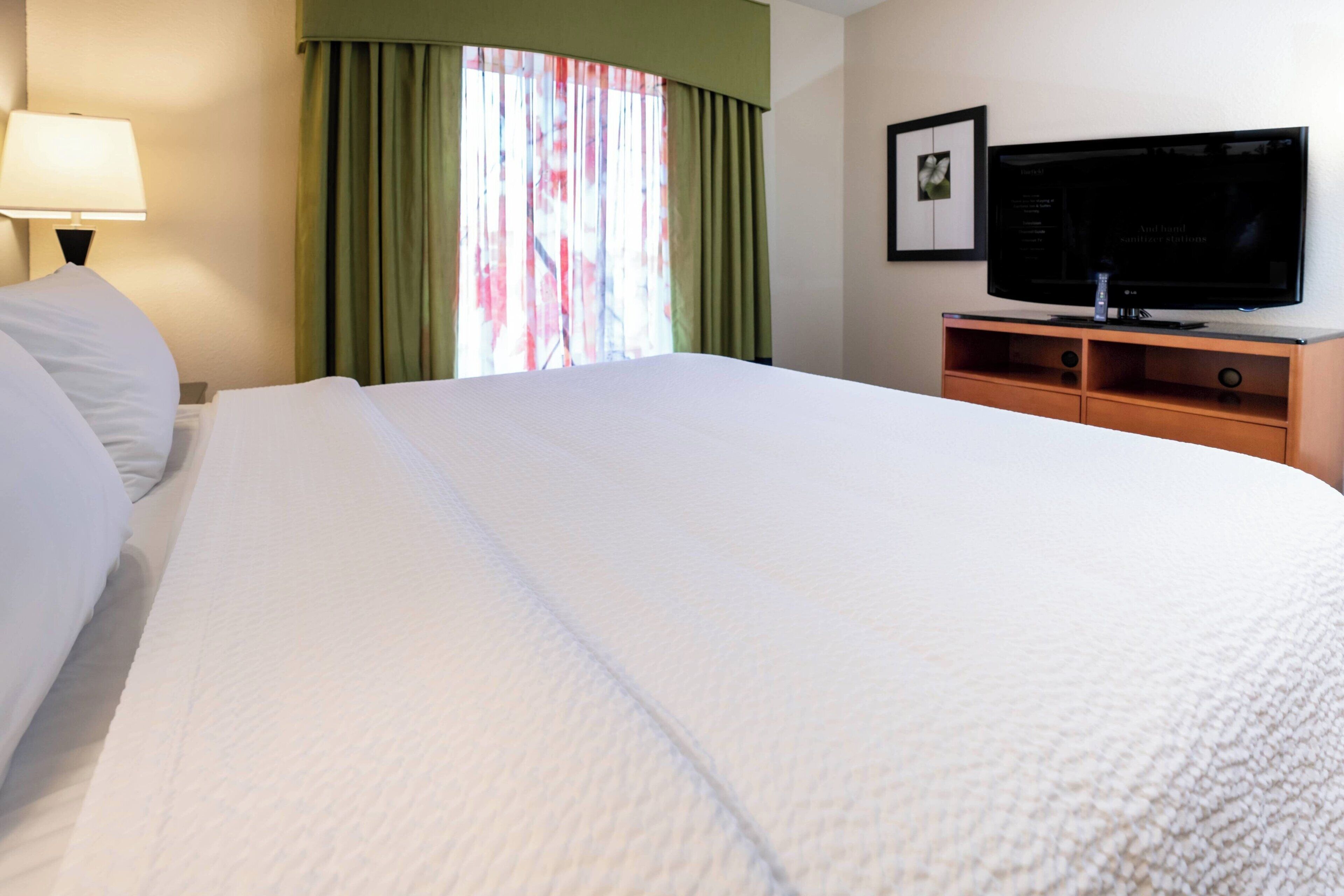Una habitación de hotel con una cama grande, un televisor sobre un mueble de madera y una ventana con cortinas.