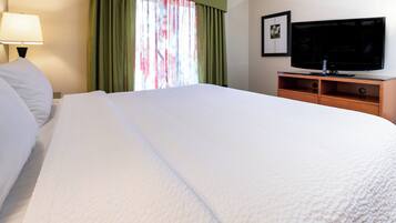 Una habitación de hotel con una cama grande, un televisor sobre un mueble de madera y una ventana con cortinas.