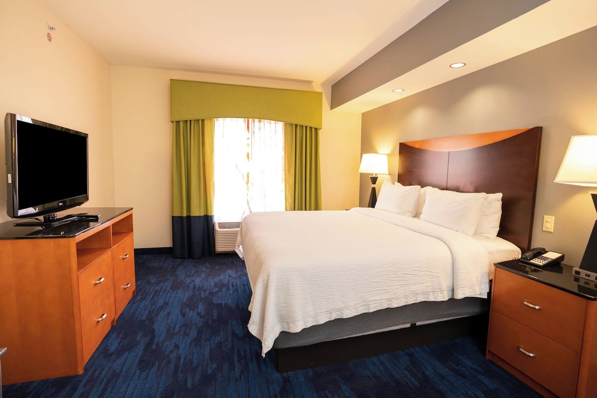 A hotel room with a bed, a TV on a wooden dresser, a desk, and a lamp.