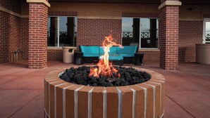 A fire pit with flames in a brick structure, surrounded by a patio area with a blue sofa and outdoor furniture. - Fairfield Inn & Suites by Marriott Kearney (Kearney)