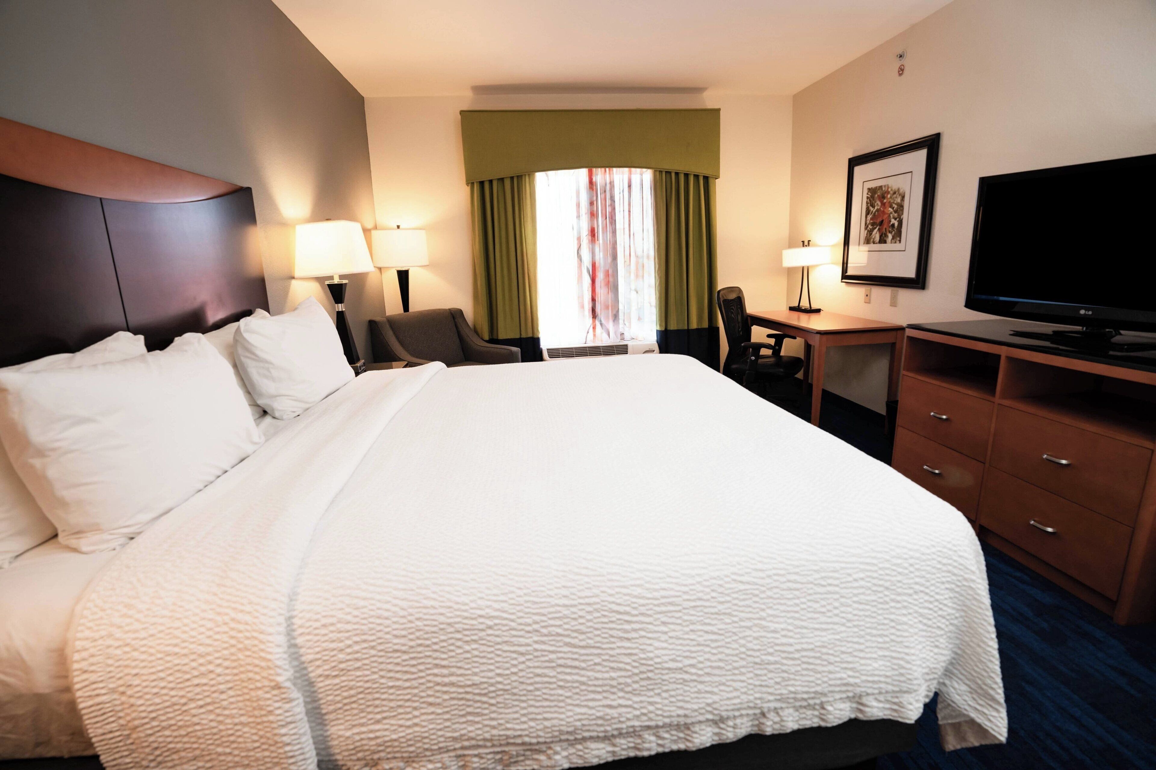 A hotel room with a large bed, a desk, a chair, a television, and a window with curtains.