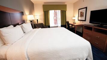 A hotel room with a large bed, a desk, a chair, a television, and a window with curtains.