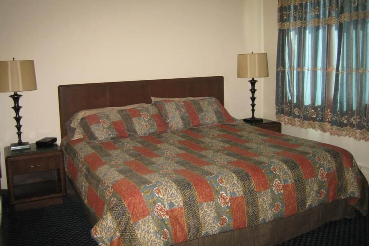 A standard hotel room with a bed, two bedside tables, lamps, and a window with curtains.