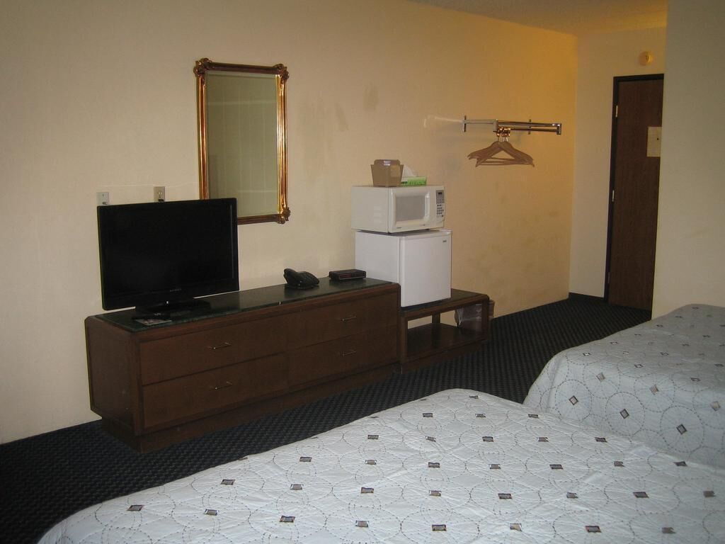Ein Hotelzimmer mit Fernseher auf einer Kommode, einer Mikrowelle, einem kleinen Tisch und zwei Betten.