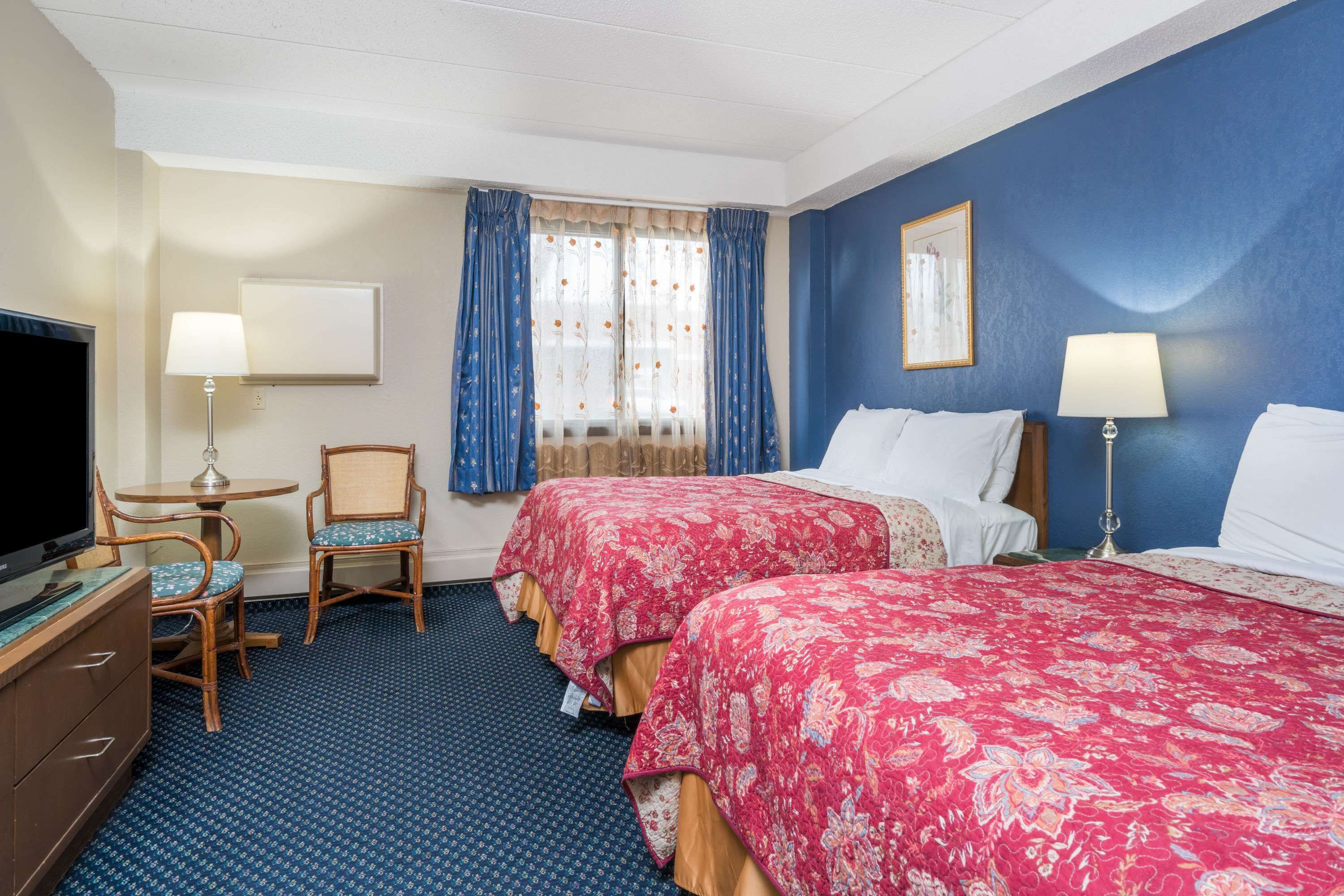 A hotel room with two beds, a television, a desk, and a chair.