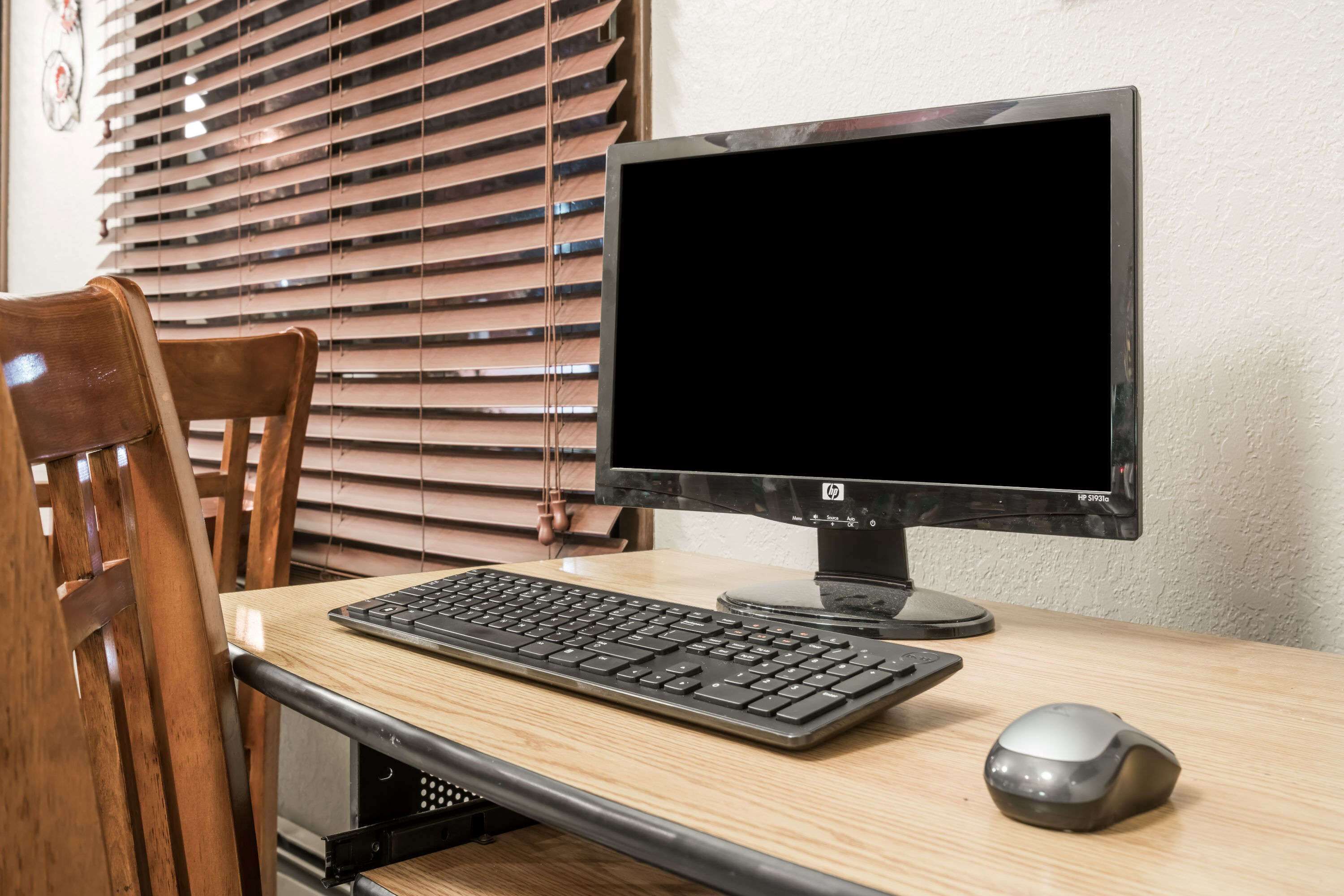 A wooden desk with a black HP monitor, keyboard, and mouse.