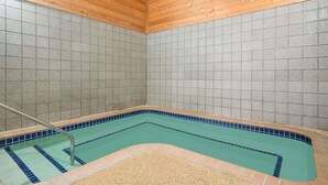 Una esquina de una habitación con un muro de azulejos, una piscina con baldosas azules y beiges, y un techo de madera.