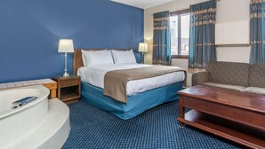Habitación de hotel con una cama grande, una mesita de noche de madera, una mesita de noche con lámparas, una alfombra azul estampada, una mesa de centro de madera y un sofá.