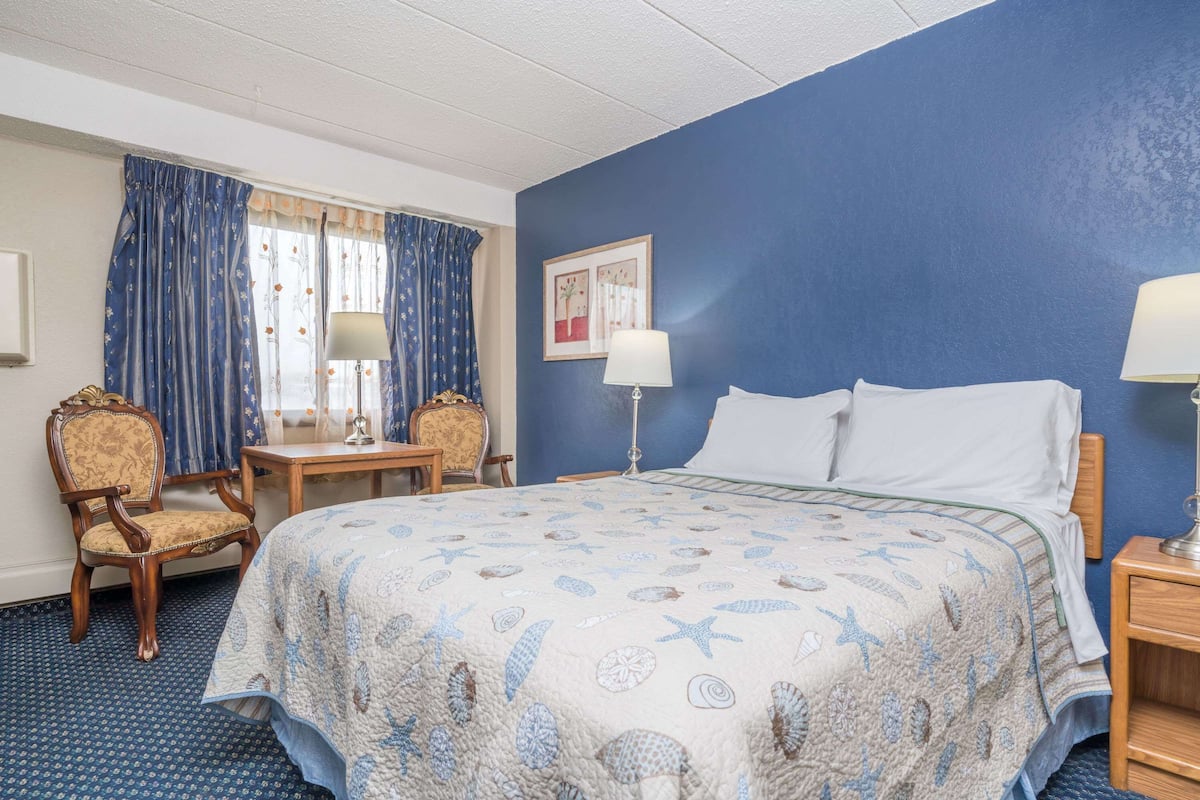 A hotel room with a large bed, a chair, a desk, and a lamp.