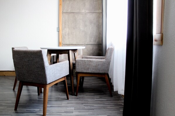 Une pièce avec une table ronde et deux fauteuils rembourrés, un mur décoratif en béton et un plancher en bois.