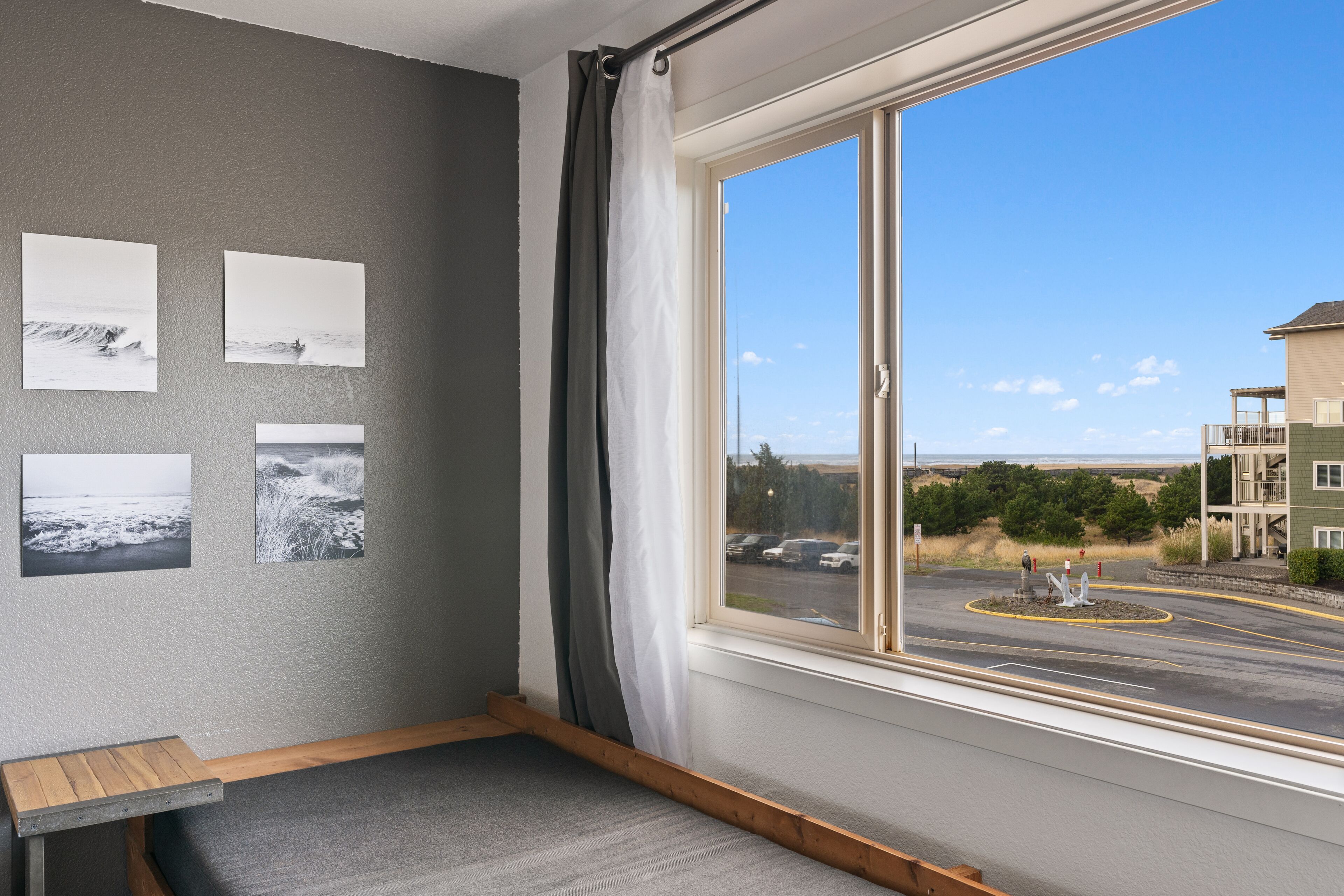 A room with a large window, grey walls, and a wooden bench.