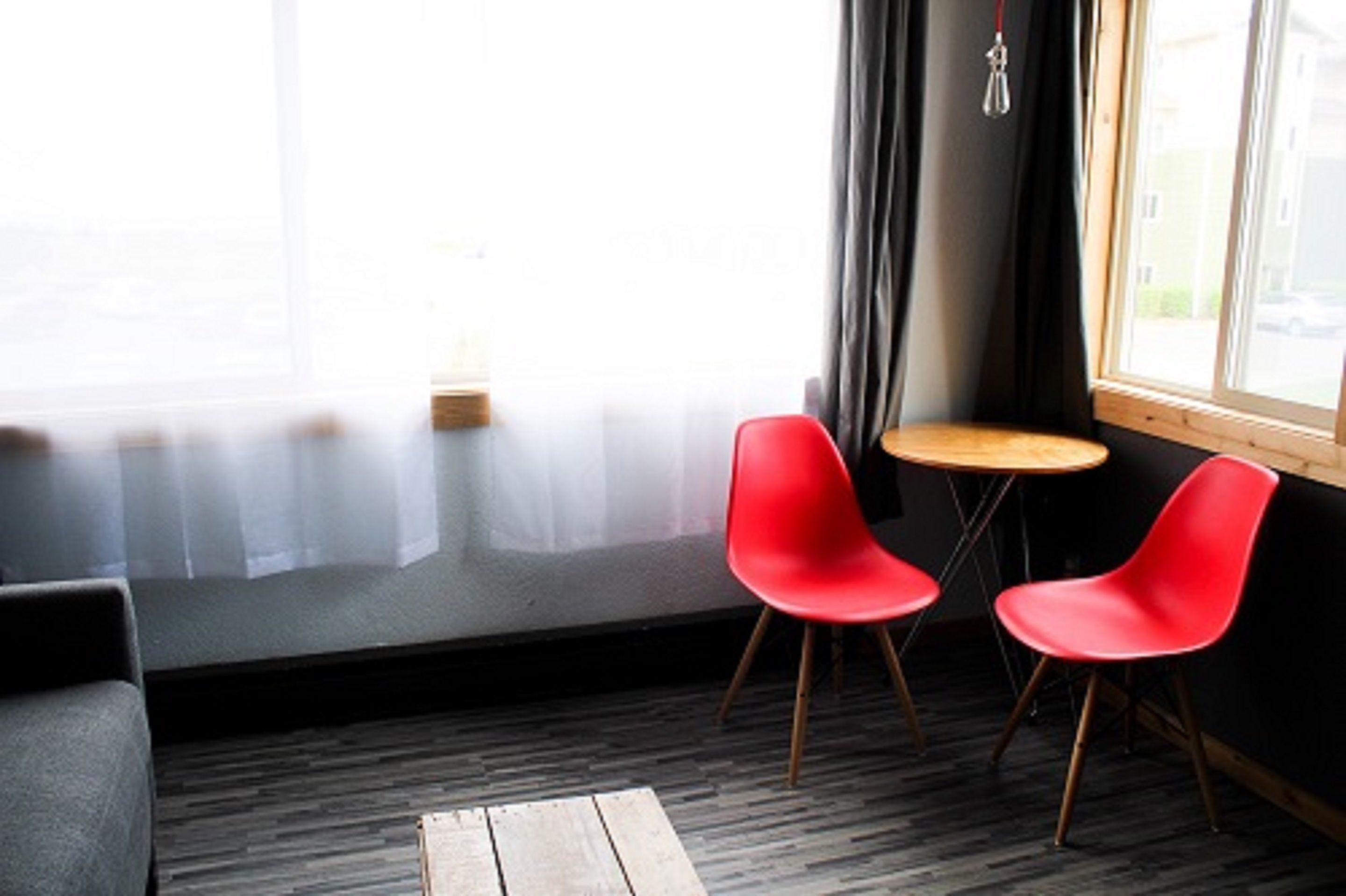 A modern room with a large window, two red chairs, a small round table, and a wooden bench.