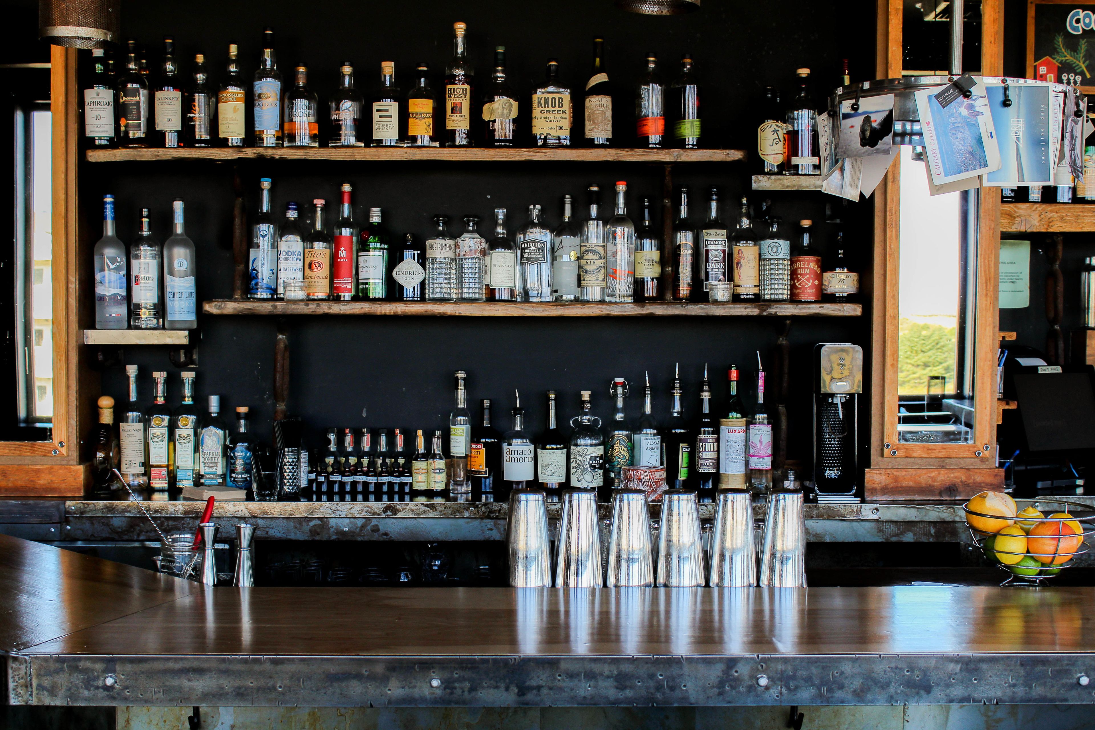 A bar with shelves of liquor bottles, a bar counter, and a fruit basket.