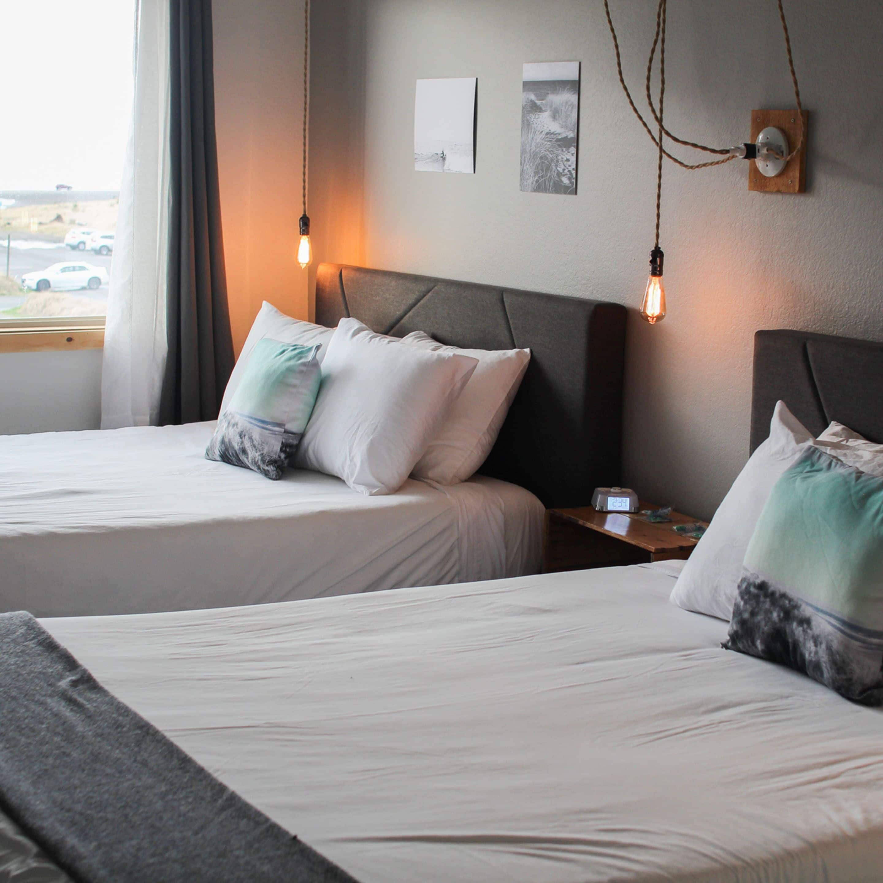 Habitación de hotel con dos camas, una mesita de noche, un reloj y obras de arte en la pared.