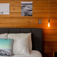 A bedroom with a wooden headboard, a bed with white and teal pillows, and a wall-mounted light fixture.