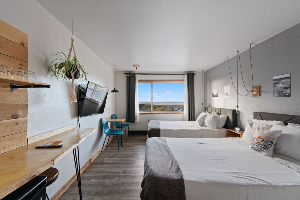 Ein Hotelzimmer mit zwei Betten, einem Schreibtisch mit Stuhl, einem Fernseher und einem großen Fenster mit Blick.