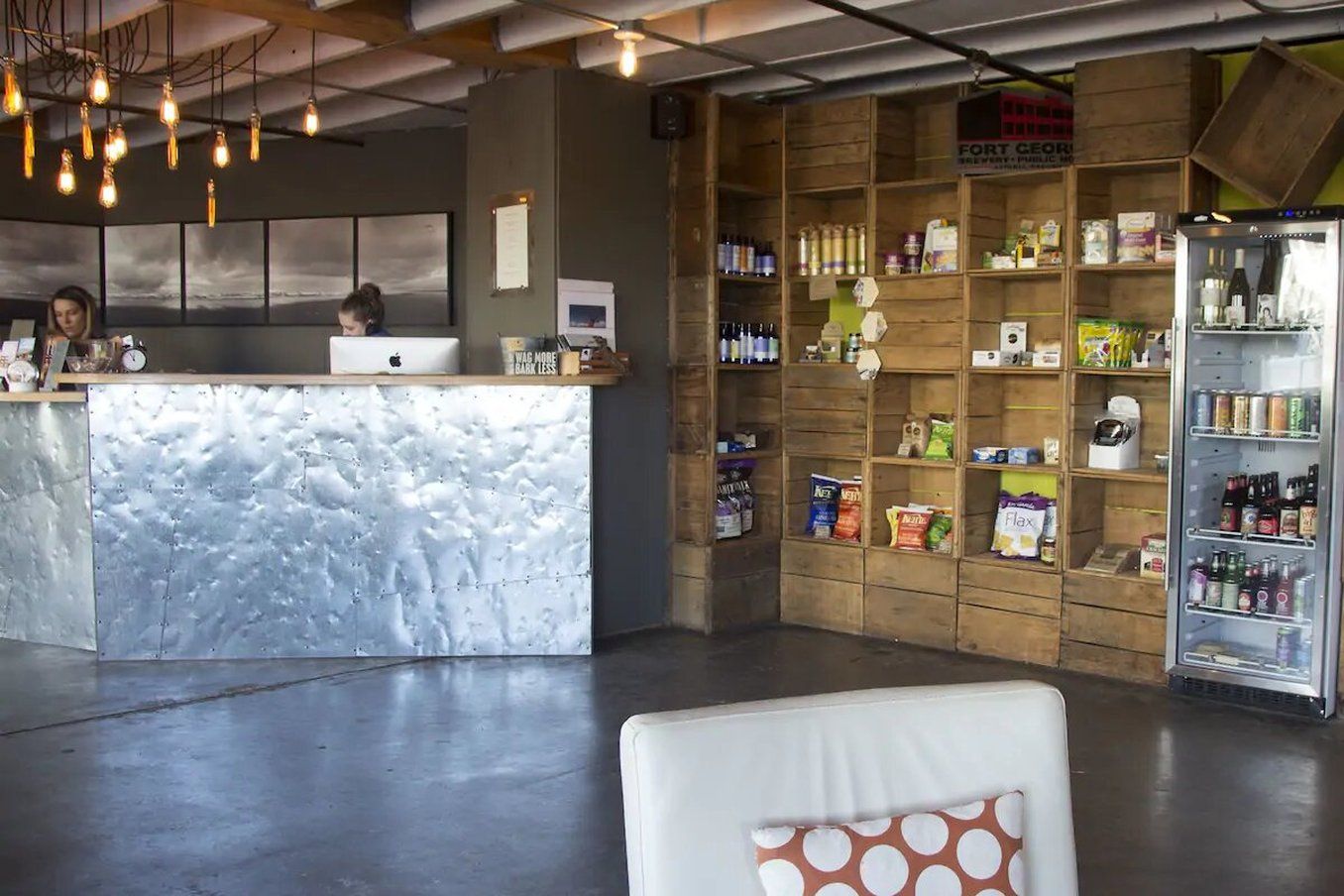 A reception area with a modern counter, wooden shelving stocked with various products, and a refrigerator.