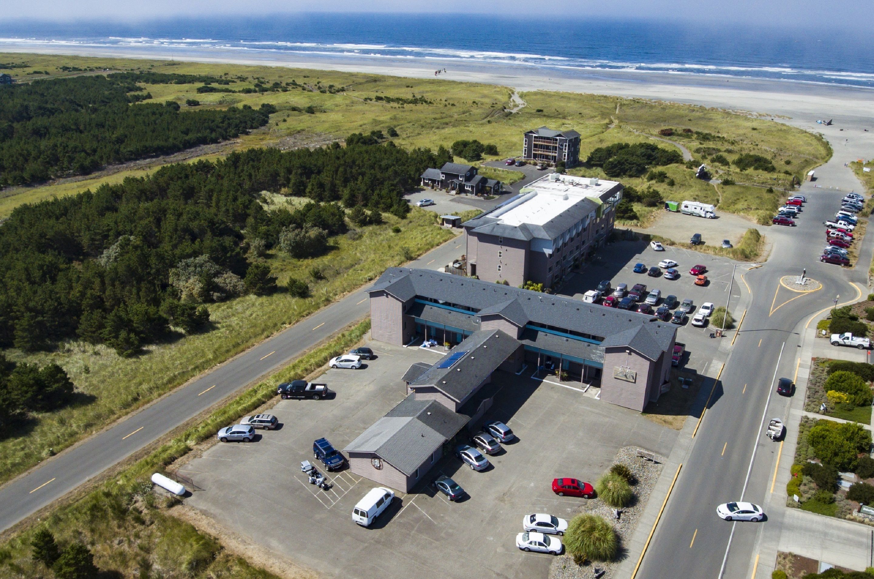 An aerial view of a building with a parking lot and a road leading to the beach.