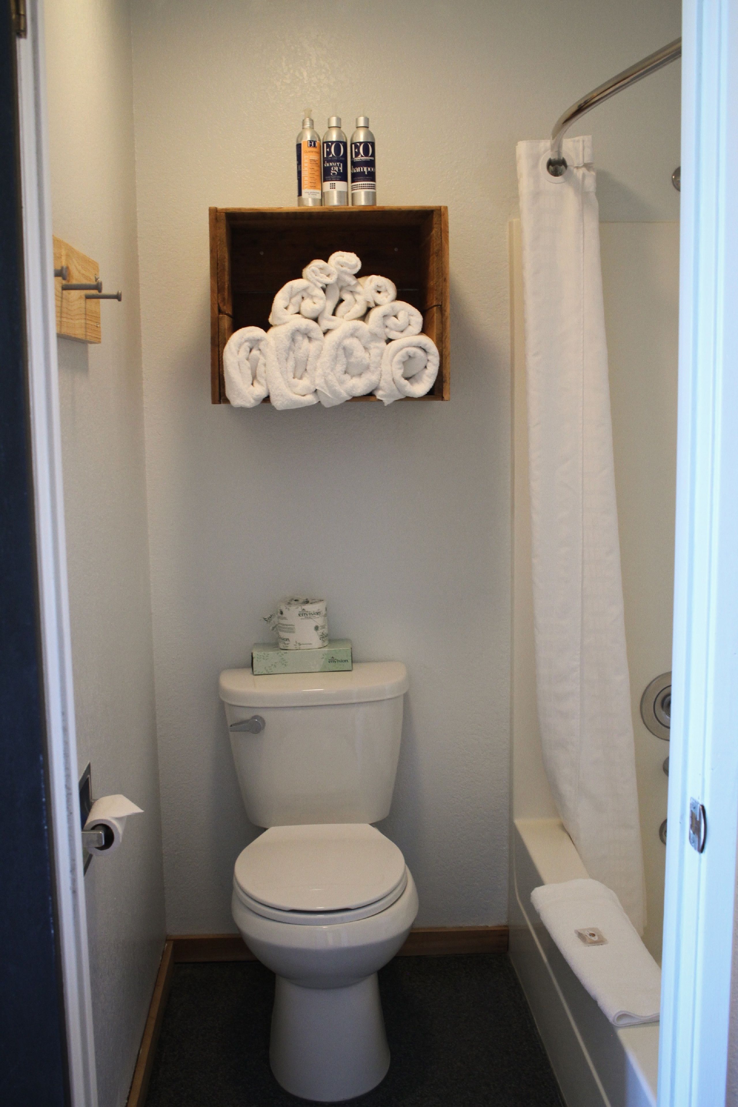 A small bathroom with a toilet, a shelf with rolled towels, and a shower curtain.