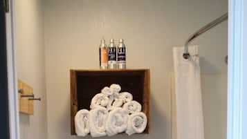A small bathroom with a toilet, a shelf with rolled towels, and a shower curtain.