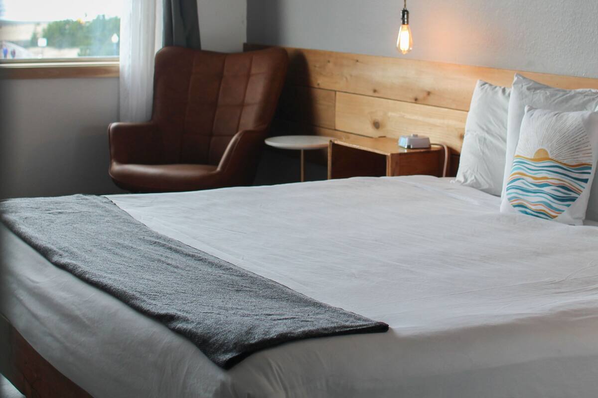 Ein Hotelzimmer mit Bett, Stuhl, kleinem Tisch und Fenster.