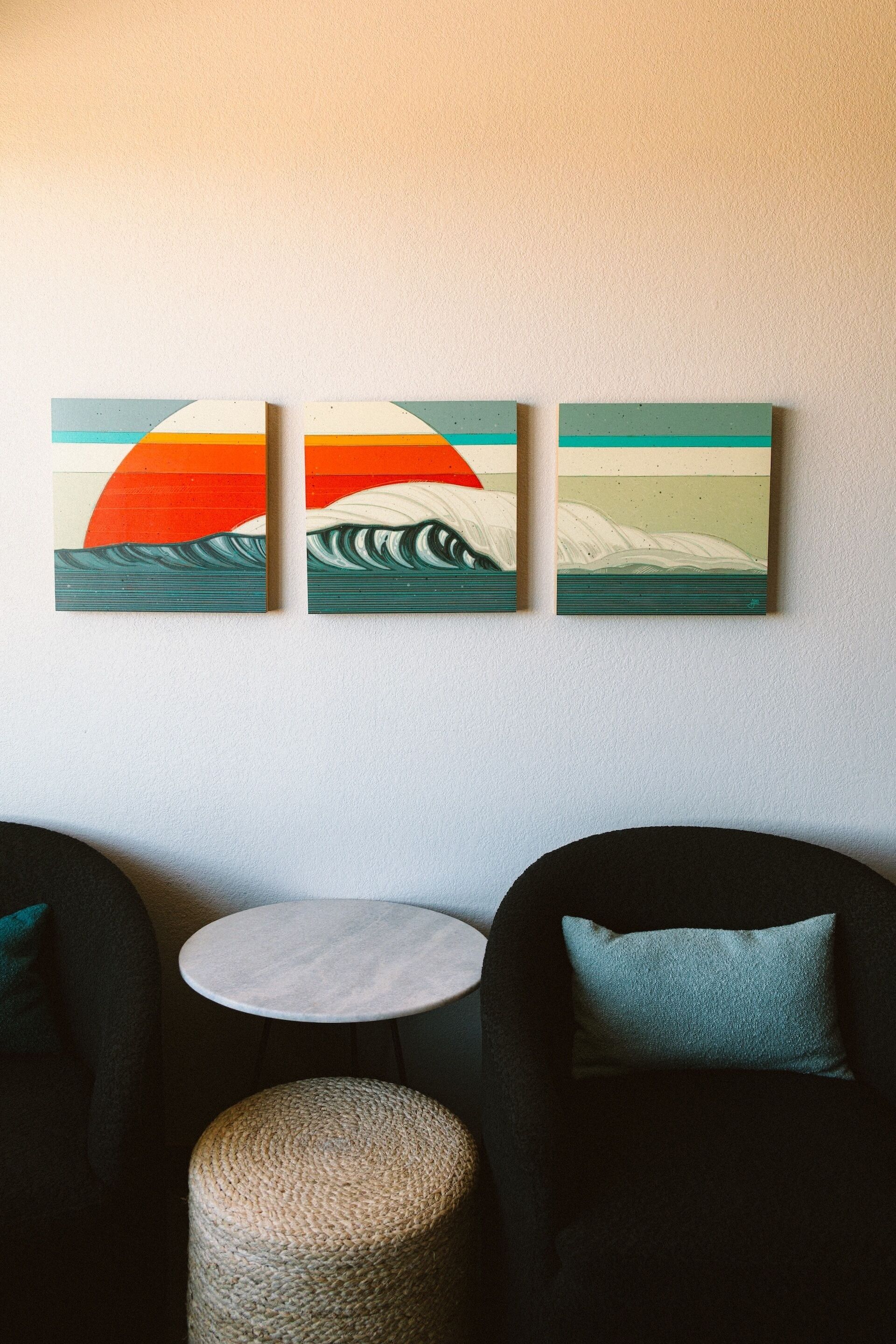 Een kamer met een ronde tafel, twee stoelen en drie schilderijen aan de muur.