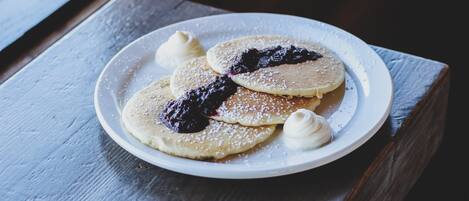 Een bord pannenkoeken met blauwe bessencompote en slagroom op een houten tafel.