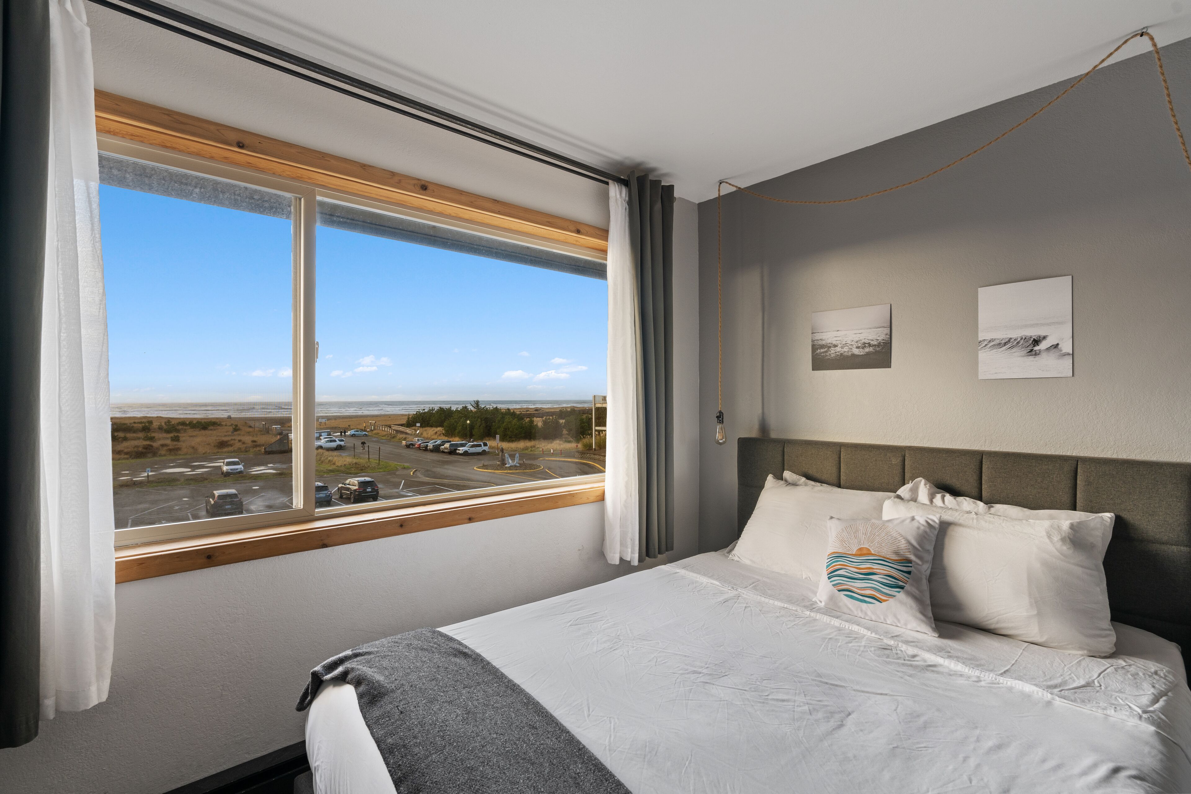 A hotel room with a large window, a bed with white bedding, and two wall-mounted pictures.