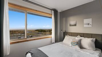 A hotel room with a large window, a bed with white bedding, and two wall-mounted pictures.