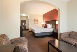 A hotel room with a large bed, two armchairs, a small table, and a nightstand.