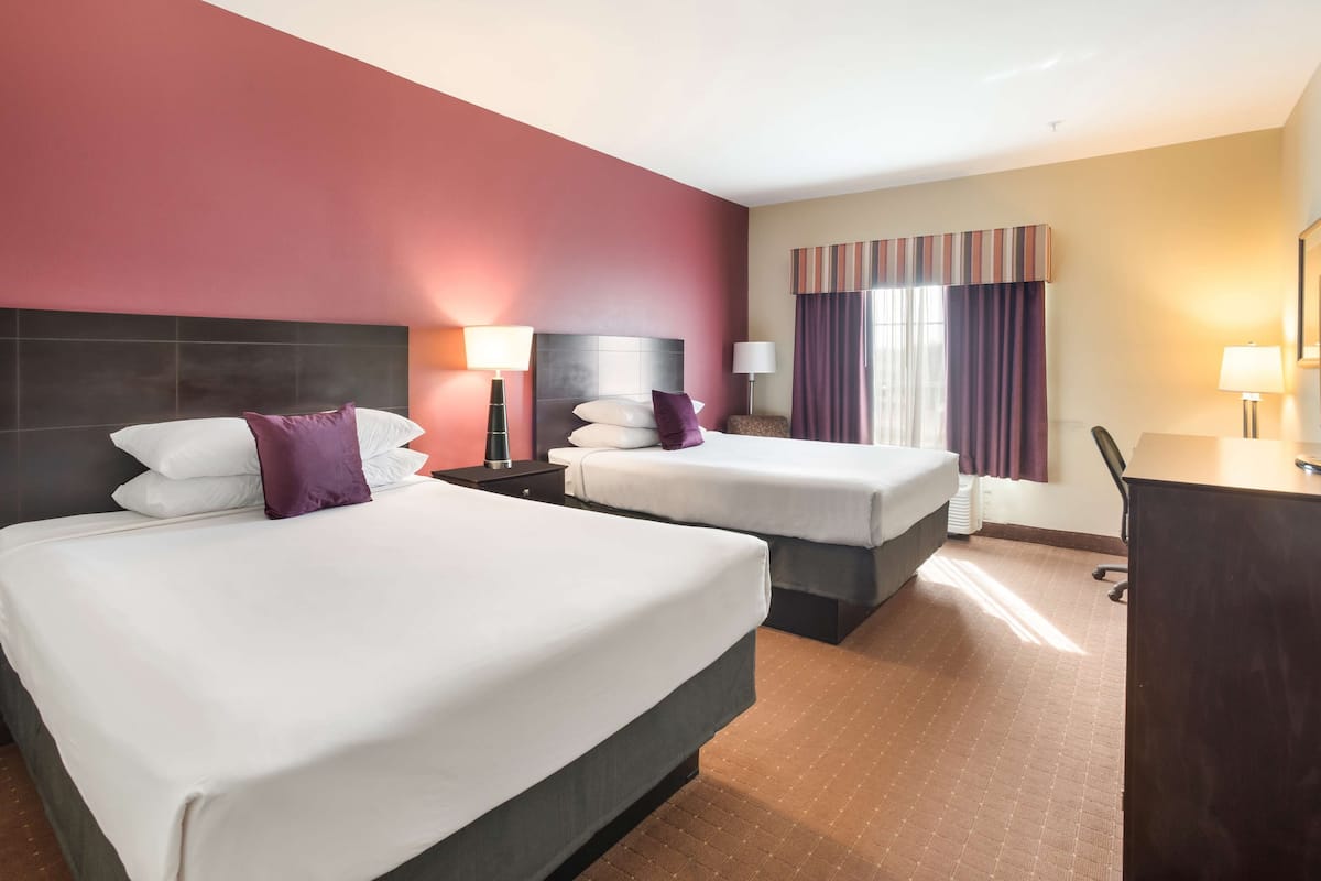 A hotel room with two beds, a desk, and a chair.