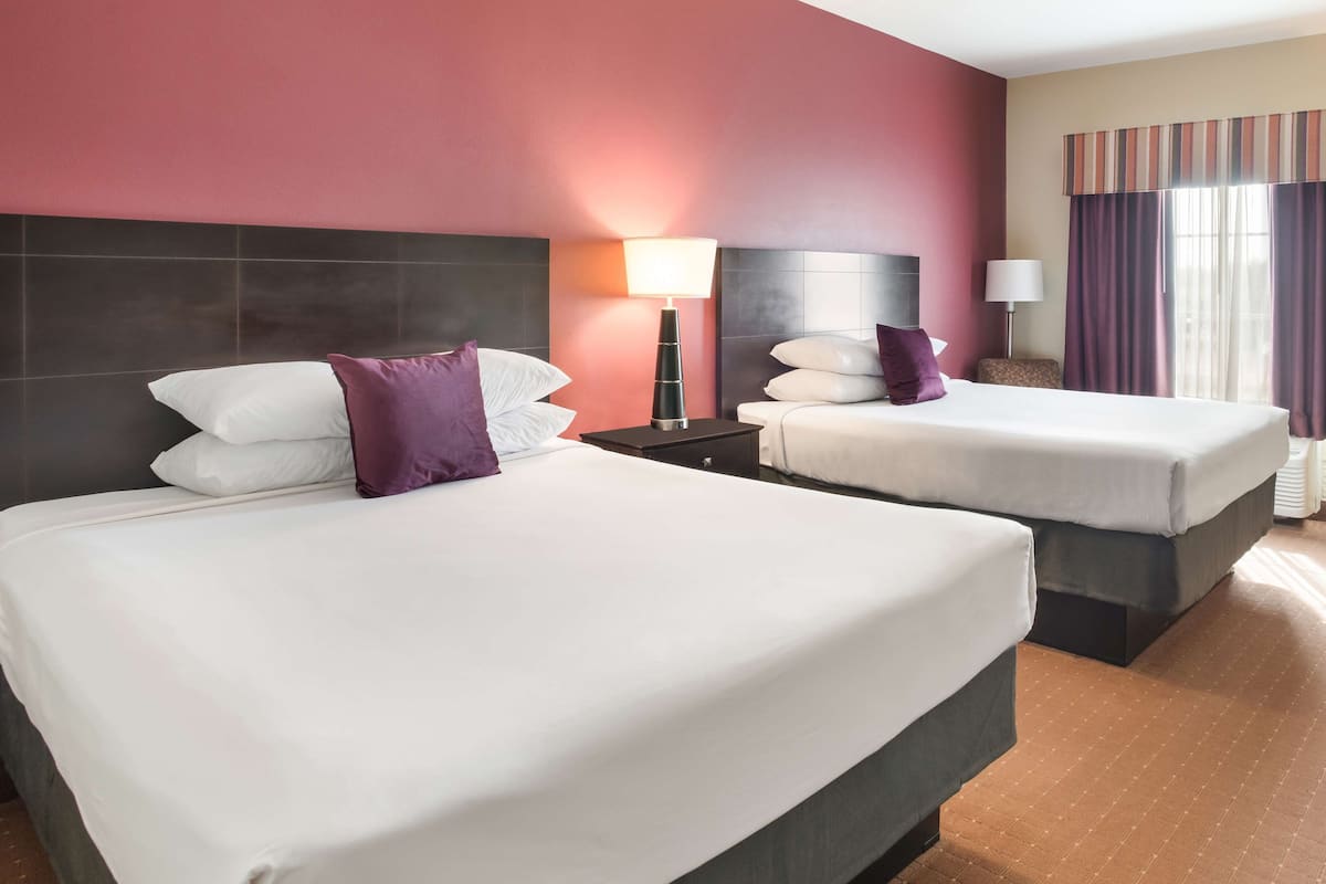 A hotel room with two beds, a nightstand with a lamp, and a window with curtains.
