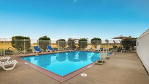A rectangular swimming pool with a metal fence, surrounded by lounge chairs and umbrellas. - Knights Inn Bunkie (Bunkie)