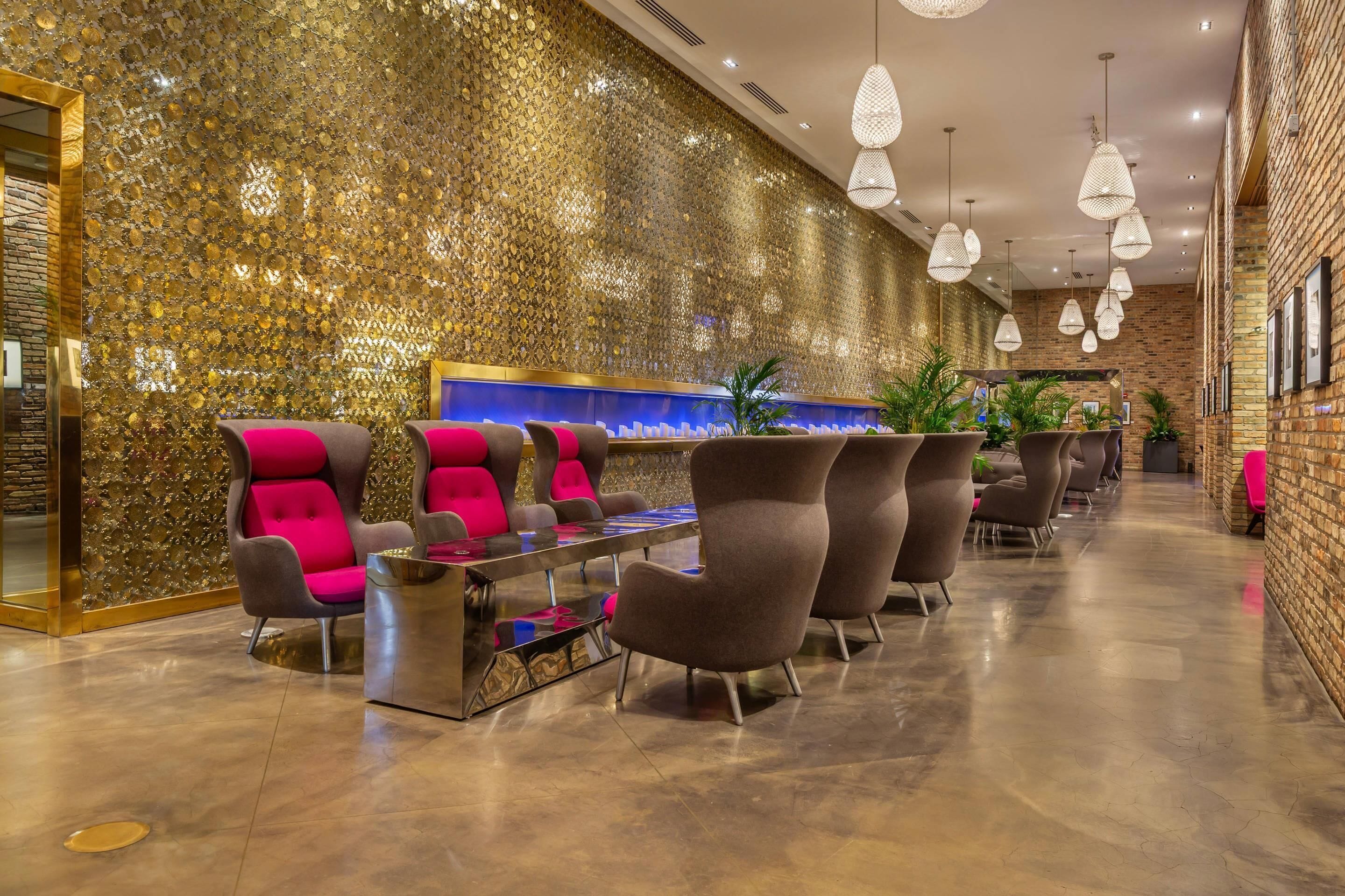 A modern lobby with a gold textured wall, seating area with chairs, a reception desk, and hanging pendant lights.