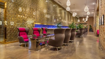 A modern lobby with a gold textured wall, seating area with chairs, a reception desk, and hanging pendant lights.