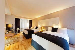 Une chambre d’hôtel avec deux lits, une télévision, un bureau avec une lampe et une fenêtre avec des rideaux.