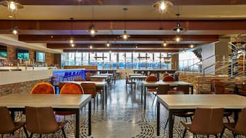 A restaurant with a bar area, multiple tables and chairs, and a view of the city through large windows.