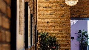A corridor with a brick wall, hanging wicker light fixture, and potted plants.