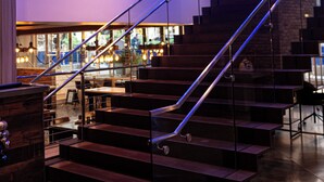 A modern interior with a staircase, glass railings, and a visible restaurant area.