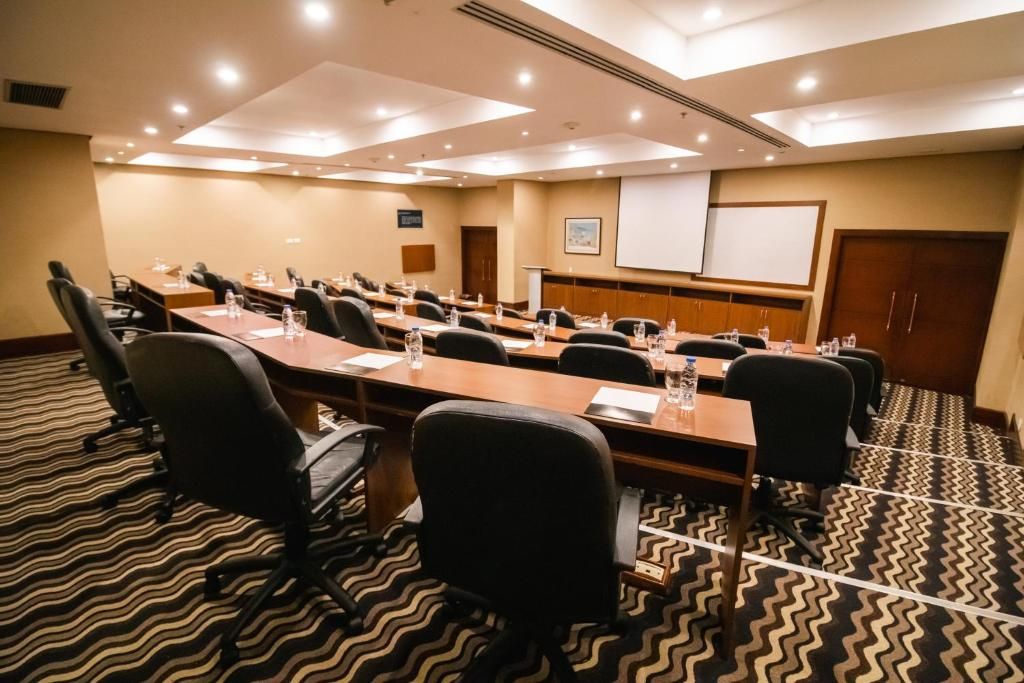 Uma sala de conferência com uma mesa comprida, várias cadeiras, uma tela de projetor e piso coberto de carpete.
