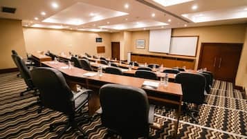 Uma sala de conferência com uma mesa comprida, várias cadeiras, uma tela de projetor e piso coberto de carpete.
