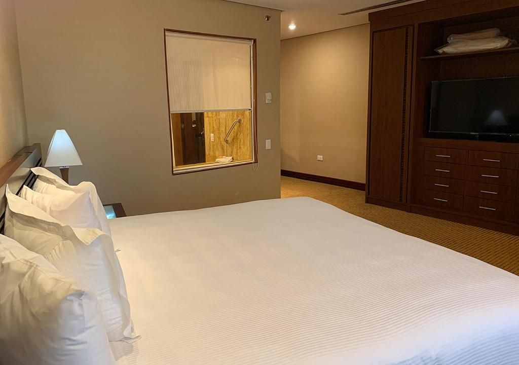 Habitación de hotel con una cama grande, televisor, ventana con persianas y un armario de madera.