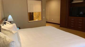 Habitación de hotel con una cama grande, televisor, ventana con persianas y un armario de madera.