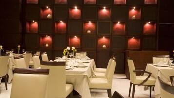 Un ristorante con diversi tavoli e sedie, ognuno apparecchiato con tovaglie bianche e candele.