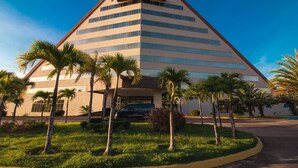 A modern building with a triangular roof and multiple floors, surrounded by palm trees and a well-maintained lawn. - Eurobuilding Hotel Plaza Guayana (Ciudad Guayana)