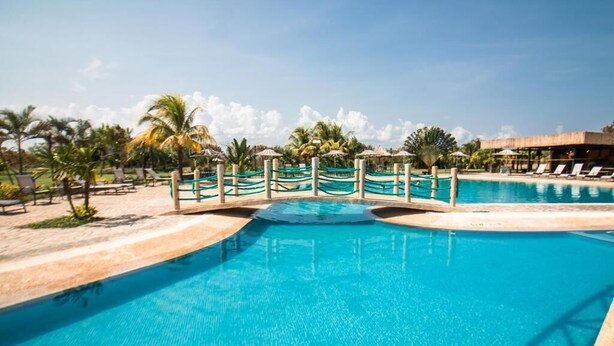 A clear blue pool with a wooden bridge, surrounded by lounge chairs and palm trees. - Eurobuilding Hotel Plaza Guayana (Ciudad Guayana)