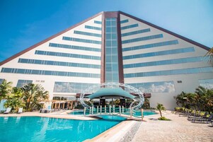 A hotel with a large swimming pool, a covered seating area, and a modern architectural design.