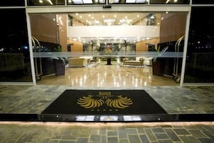 Um saguão de hotel com uma recepção central, área de estar e um emblema decorativo no chão.