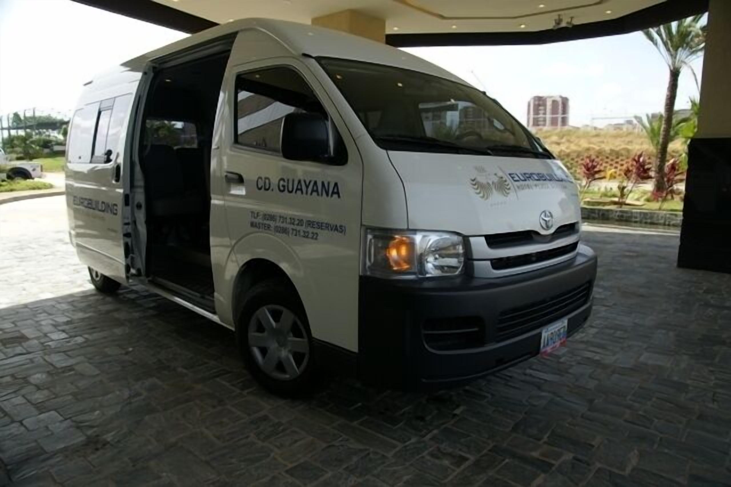 A white van with "CD. GUAYANA" and "EUROBUILDING" on the side, parked on a paved area with a building in the background.